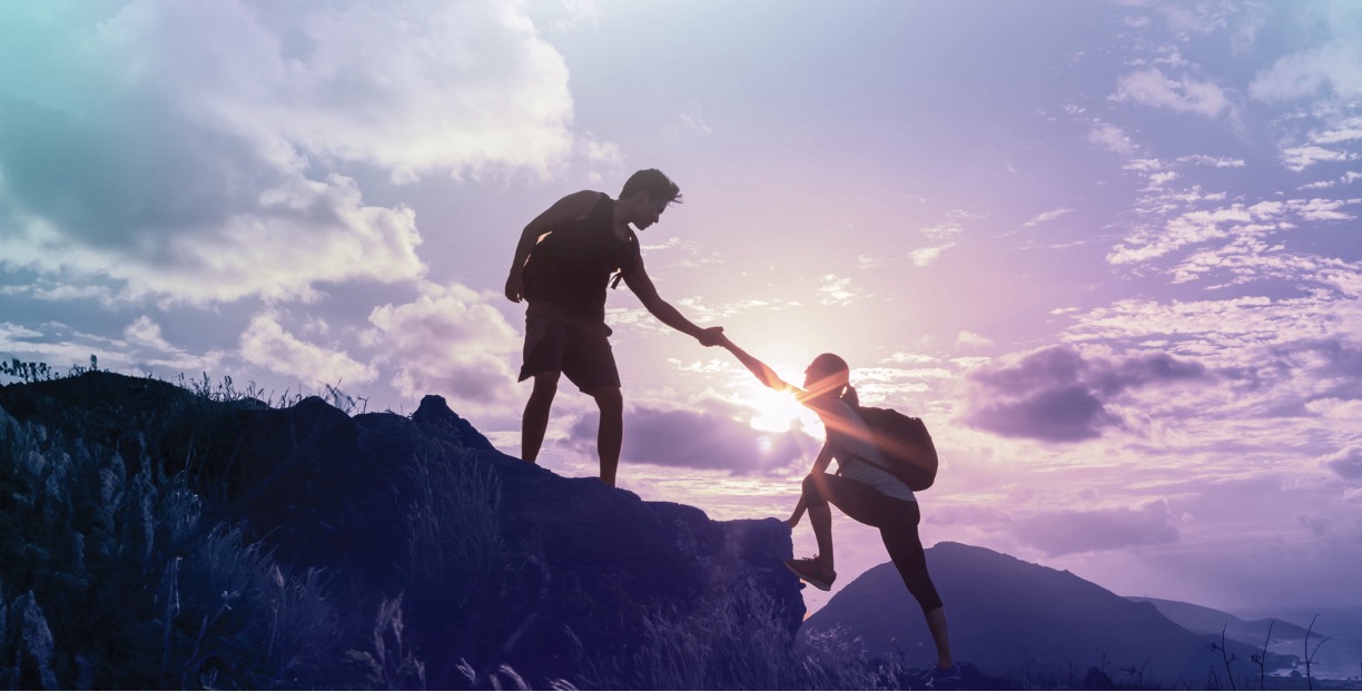 One hiker helping another climb a mountain, symbolising how intentional financial planning can help build and protect long-term wealth.