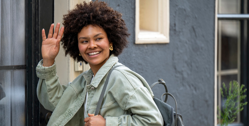 Young adult waving goodbye while standing outside a home with a backpack, symbolising independence, life transitions and the start of a new chapter for both children and parents – the empty nest.