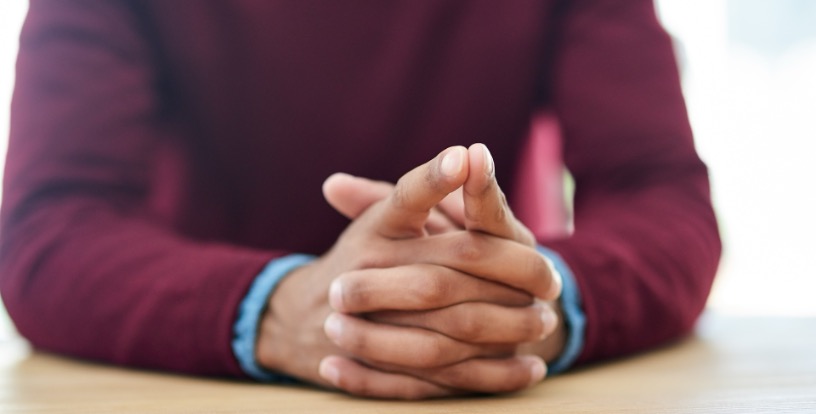 Person sitting with hands clasped on a table, representing reflection, financial well-being and the personal relationship between money, mindset and peace of mind.